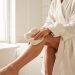 Femme appliquant une mousse autobronzante sur sa jambe avec un gant dans une salle de bain lumineuse et élégante.