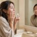 Femme de plus de 40 ans appliquant délicatement un sérum sur son visage devant un miroir dans une salle de bain lumineuse.